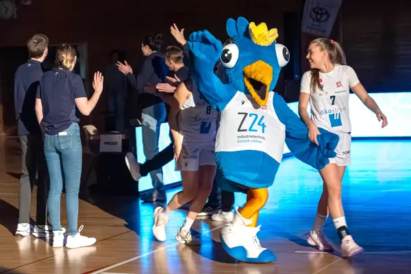Das Maskottchen Birdie läuft mit den Basketballspielerinnen auf das Basketballspielfeld und winkt den Zuschauern zu.