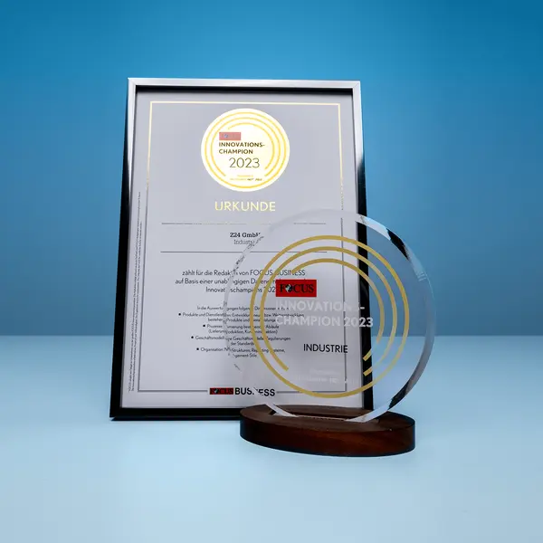 Gerahmte Urkunde und transparente Trophäe mit der Aufschrift "FOCUS Innovationschampion 2023" auf einem Tisch, vor blauem Hintergrund.