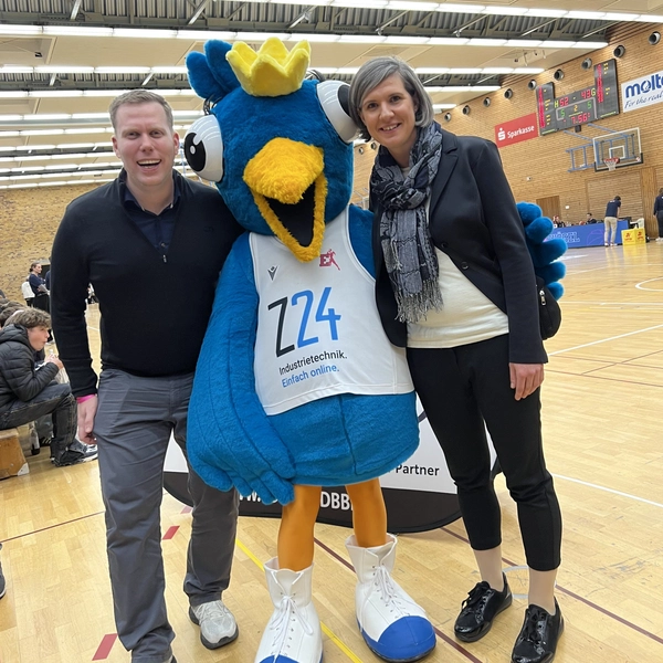 Das Maskottchen Birdie steht zwischen Michael Ebner-Seibold und Tabea Seibold in der Sporthalle der Eisvögel Freiburg.