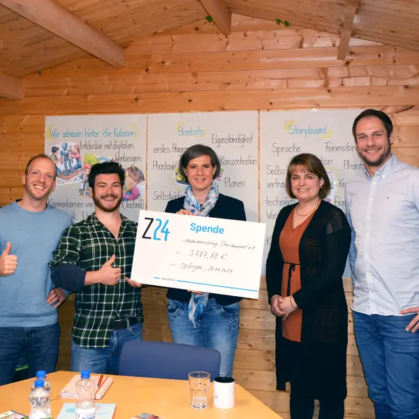5 Personen stehen in einer Reihe und schauen freundlich in die Kamera. Die Geschäftsführerin Tabea Seibold hält einen Spendencheck der Z24 GmbH in der Hand. Im Hintergrund hängen Plakate von Kindern aus einem Kindergarten.