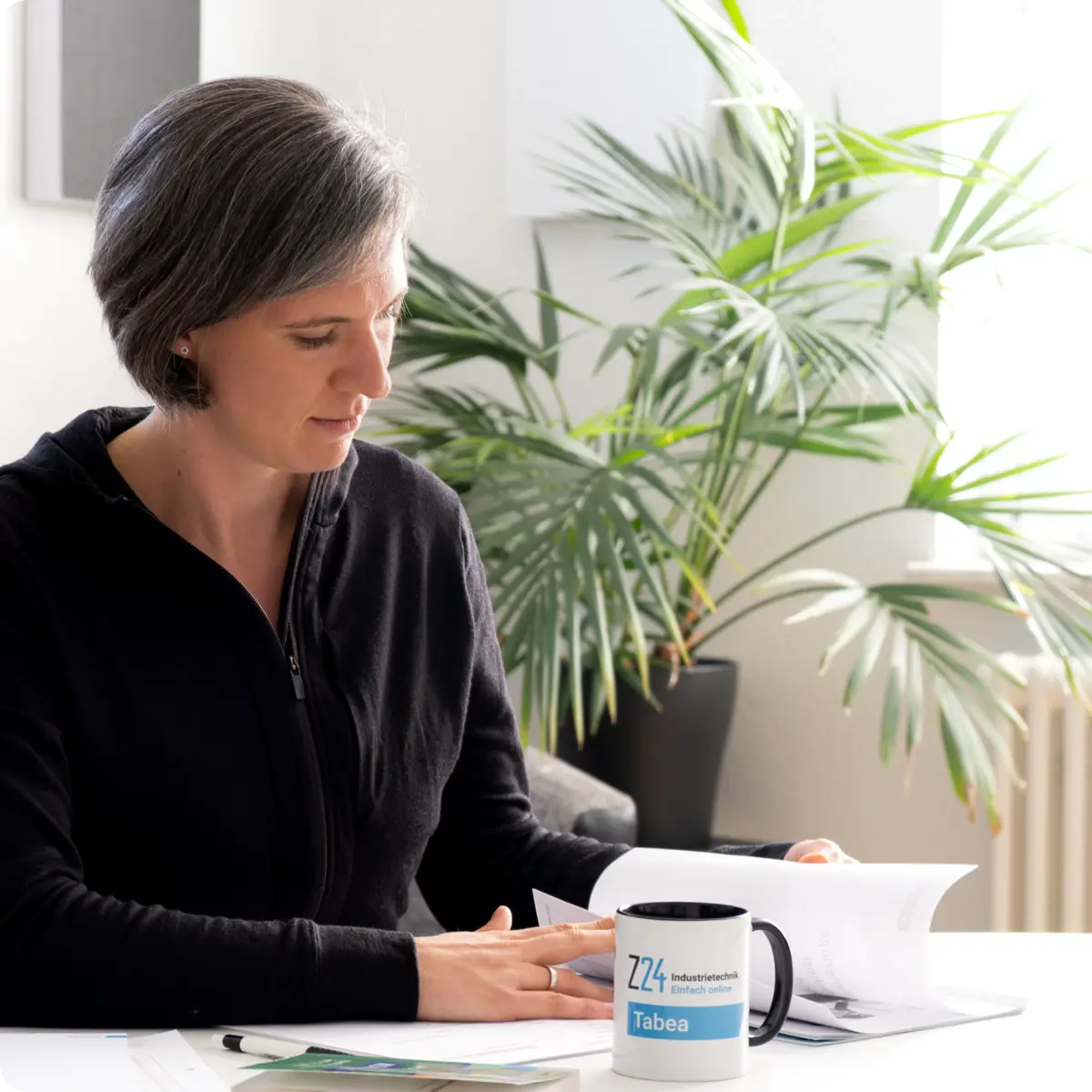 Frau Tabea Ebner-Seibold sitzt an einem Tisch mit ihren Unterlagen und blättert diese durch. Daneben liegt ein Buch "Kompaktwissen Kaufleute im E-Commerce" und die Z24-Tasse mit Aufschrift "Tabea".