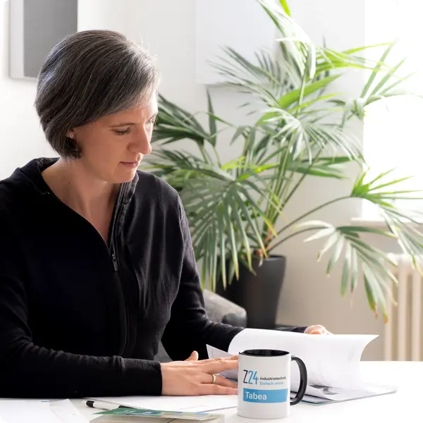 Frau Tabea Seibold sitzt an einem Tisch mit Ihren Unterlagen und blättert diese durch. Daneben liegt ein Buch "Kompaktwissen Kaufleute im E-Commerce" und die Z24 Tasse von Tabea Seibold.