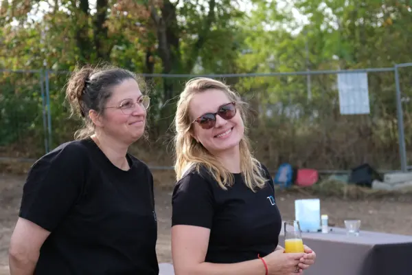 Zwei Frauen in schwarzen T-Shirts mit dem Z24-Logo stehen auf dem neuen Grundstück der Z24 GmbH. Frau rechts hält ein Glas Orangensaft und im Hintergrund ist ein Tisch zu sehen.