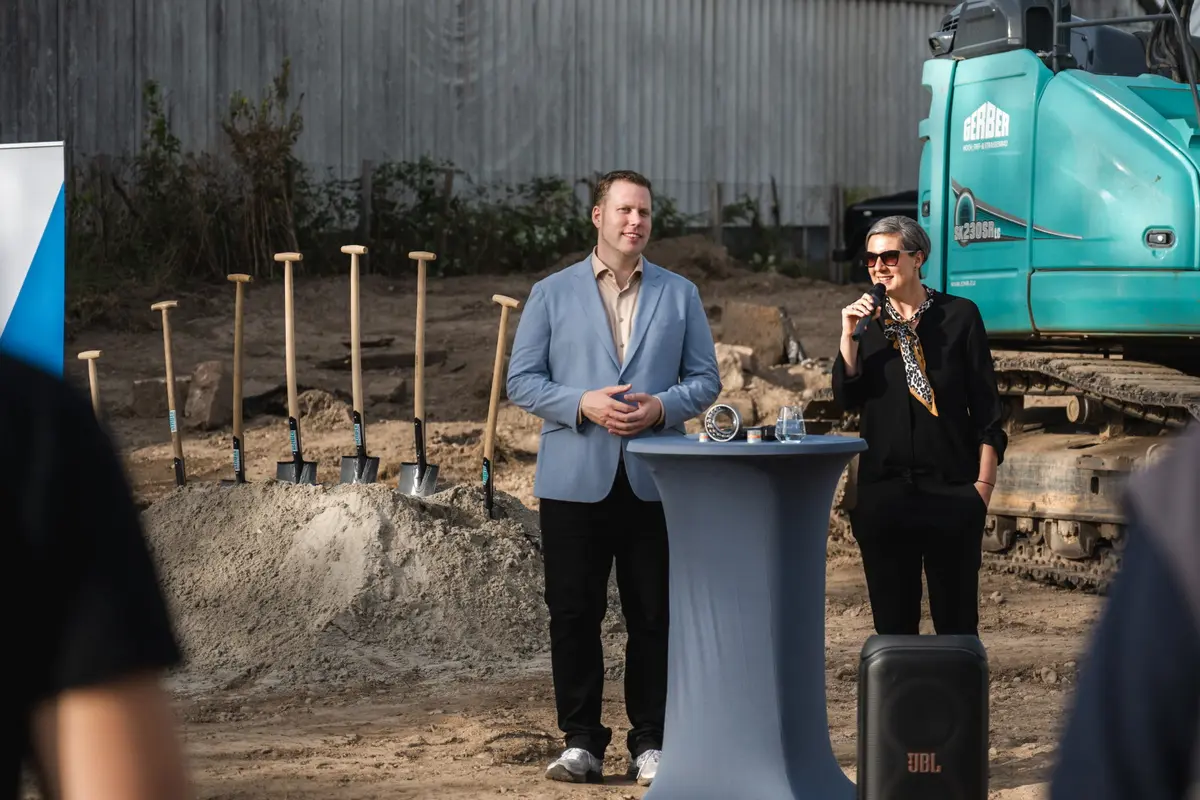Michael Ebner-Seibold und Tabea Ebner-Seibold stehen nebeneinander vor einem Bagger auf dem neuen Firmengelände der Z24 GmbH und halten eine Rede.