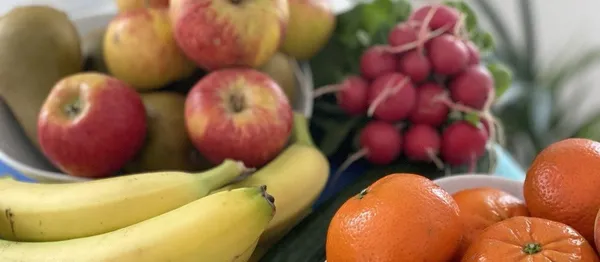 Ein Arrangement aus frischem Obst und Gemüse, darunter Bananen, Äpfel, Mandarinen, Radieschen und eine Gurke.