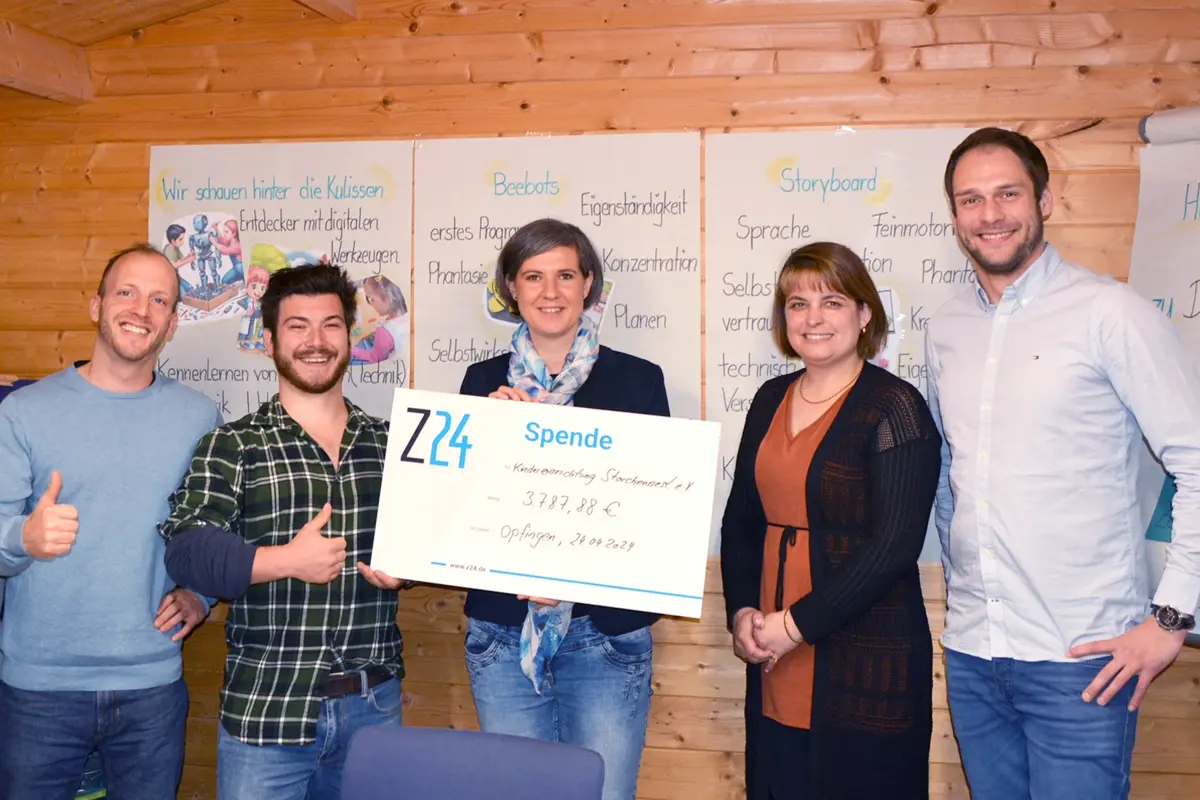 5 Personen stehen in einer Reihe und schauen freundlich in die Kamera. Die Geschäftsführerin Tabea Ebner-Seibold hält einen Spendencheck der Z24 GmbH in der Hand. Im Hintergrund hängen Plakate von Kindern aus einem Kindergarten.
