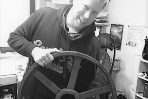 Ein Mann hält ein großes Zahnrad in einem Büro, umgeben von Schreibtischmöbeln und einem Stuhl.
