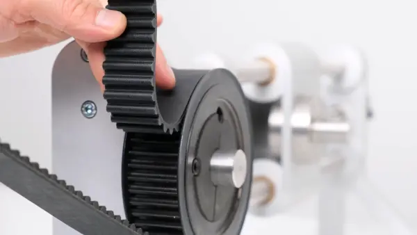 Zahnriemen wird von Hand in eine Zahnscheibe eingesetzt; die Verzahnung von Riemen und Scheibe ist deutlich sichtbar.