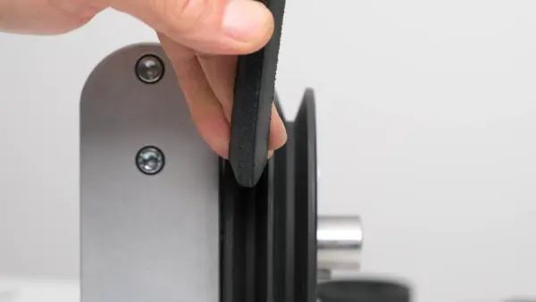 Nahaufnahme einer Riemenscheibe mit V-förmiger Nut, in die ein schwarzer Keilriemen von Hand eingesetzt wird.