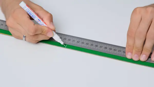 Markierung wird mit einem Stift entlang eines Metalllineals auf einem grünen Antriebsriemen angebracht, um eine definierte Mess- oder Schnittlänge festzulegen.