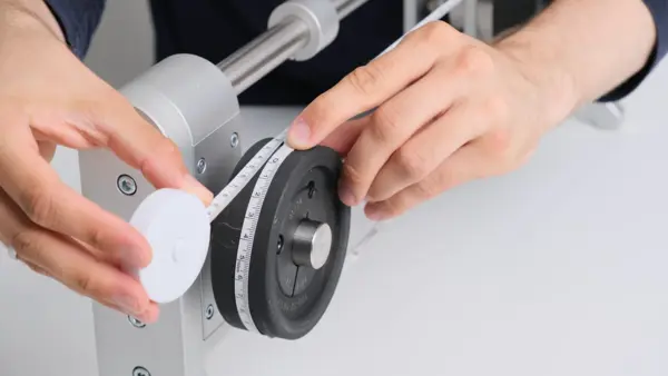 Riemenbreite wird an einem gespannten Antriebsriemen auf einer Riemenscheibe mithilfe eines Messstreifens manuell überprüft.