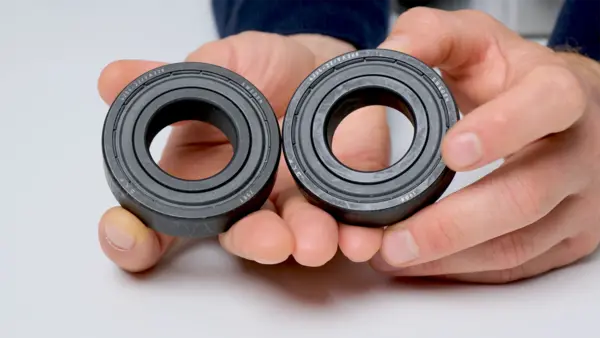 Zwei Kugellager mit schwarzer Dichtung werden nebeneinander in beiden Händen gehalten und zum Vergleich präsentiert.