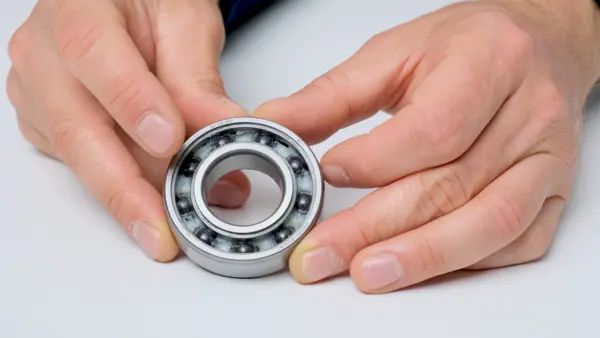 Offenes Kugellager mit sichtbaren Stahlkugeln wird von zwei Händen auf einem hellen Untergrund gehalten und ausgerichtet.