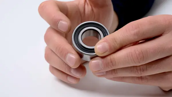 Kugellager mit schwarzer Dichtung wird zwischen Daumen und Fingern gehalten und frontal präsentiert.