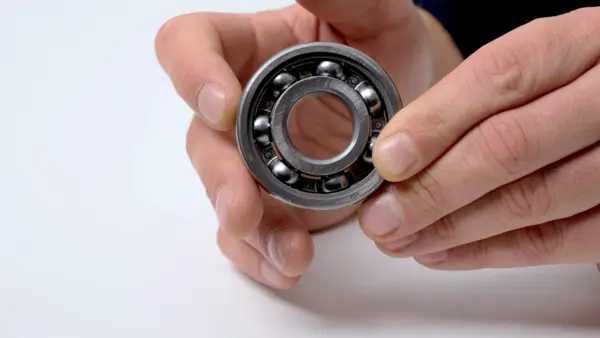 Offenes Kugellager mit sichtbaren Stahlkugeln wird zwischen Daumen und Fingern gehalten und frontal gezeigt.