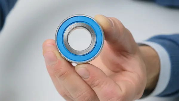 Kugellager mit blauer Dichtung wird zwischen Daumen und Fingern gehalten und frontal gezeigt