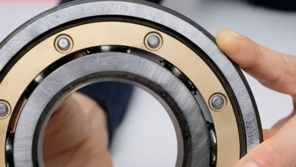 Detailaufnahme eines offenen Kugellagers mit sichtbarem Käfig und Stahlkugeln; das Lager wird von Hand gehalten und seitlich gezeigt.