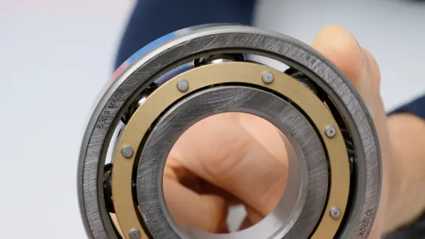 Nahaufnahme eines offenen Kugellagers mit sichtbar montiertem Käfig und Stahlkugeln; das Lager wird von Hand gehalten und frontal gezeigt.