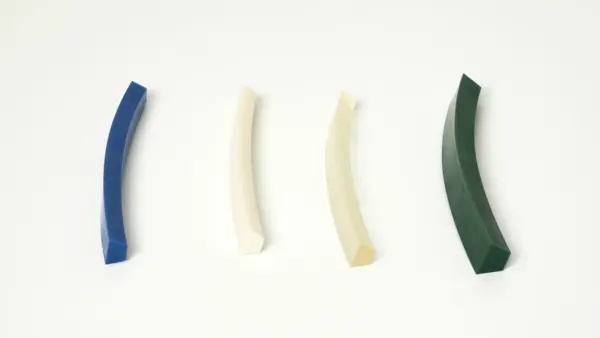 Vier unterschiedlich farbige Keilriemenabschnitte (blau, weiß, beige und grün) nebeneinander auf einer weißen Fläche zur Darstellung verschiedener Riemenmaterialien und -profile.