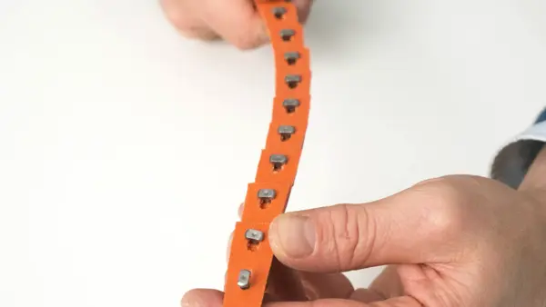 Nahaufnahme eines orangefarbenen Keilriemens, der mit einer Reihe von metallischen mechanischen Verbindern zusammengehalten wird.