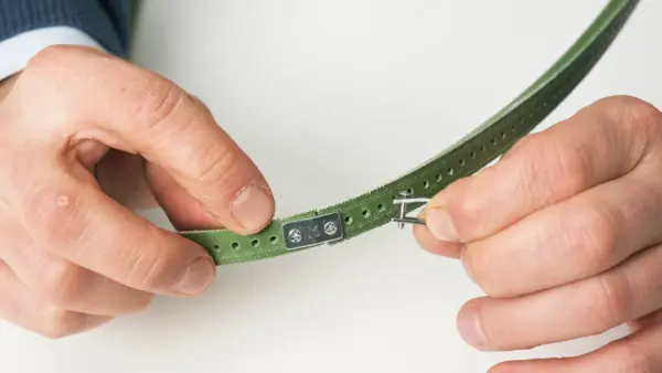 Nahaufnahme von Händen, die einen grünen Keilriemen mit mechanischem Verbindungsstück zusammenfügen.