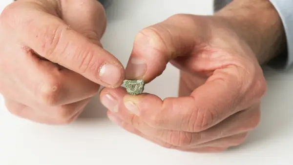 Nahaufnahme von Händen, die ein abgeschnittenes Endstück eines grünen Keilriemens mit sichtbarer Gewebe- und Verstärkungsschicht halten.