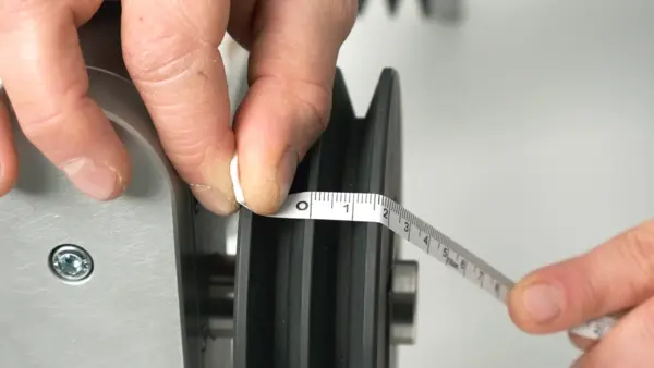 Eine Person misst mit einem Maßband die Breite einer Riemenscheibe an einer Maschine.