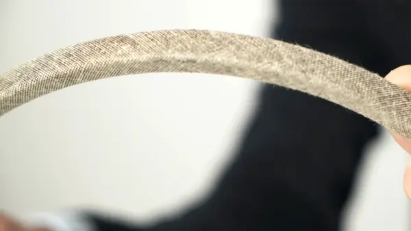 Nahaufnahme eines Keilriemens mit Gewebe- oder Stoffummantelung, der von einer Person in den Händen gehalten wird.