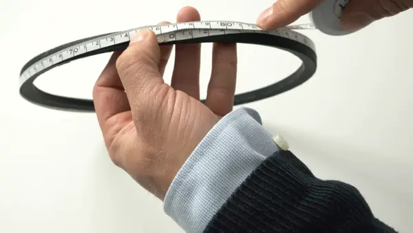 Person hält einen Keilriemen in den Händen und misst ihn mit einem Maßband.