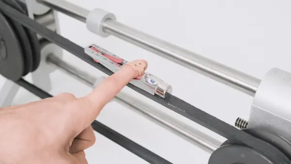 Hand zeigt auf einen Spannungsmesser, der auf einem Keilriemen angebracht ist, um die richtige Riemenspannung zu überprüfen.