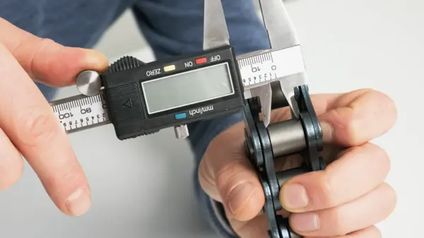 Eine Person misst mit einer digitalen Schieblehre den Durchmesser einer Rolle an einer Industriekette.