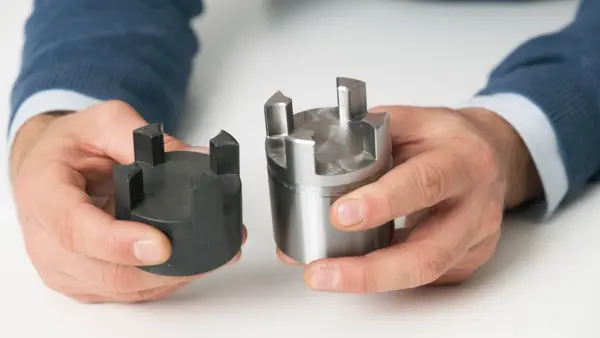Eine Person hält zwei Kupplungsnaben aus unterschiedlichen Materialien – eine schwarze aus Stahl und eine silberne aus Metall – in den Händen zum Vergleich.