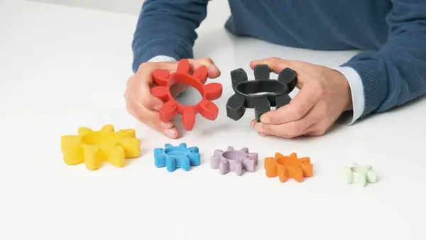 Eine Person hält zwei Kupplungskränze in Rot und Schwarz, während mehrere weitere farbige Varianten in unterschiedlichen Größen auf dem Tisch liegen.