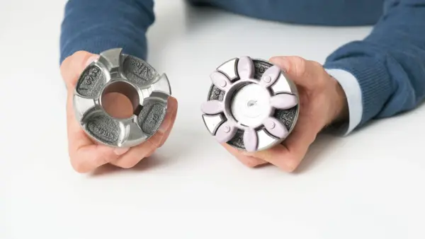 Zwei Hände halten zwei Hälften einer Metallklauenkupplung, eine davon mit einem eingesetzten elastischen Kupplungskranz aus Kunststoff.