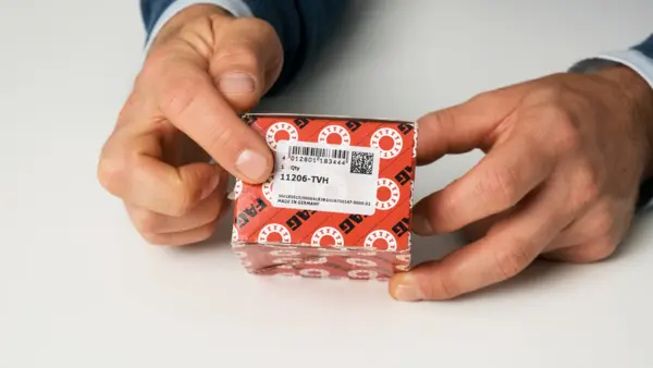 Eine Hand zeigt auf das Etikett einer rot-weißen FAG-Verpackung mit Produktnummer.