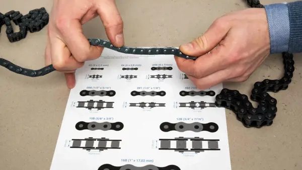 Zwei Hände spannen eine Rollenkette über eine Z24-Profilübersicht, um die Kettenteilung mit den abgebildeten Profilen zu vergleichen und die passende Größe zu bestimmen.