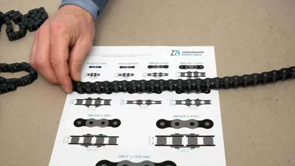 Hand legt eine Rollenkette auf eine Profilübersicht von Z24 Industrietechnik, um die passende Kettenteilung zu bestimmen.