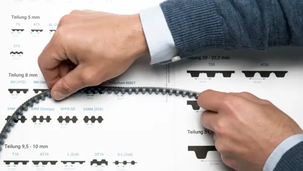 Zwei Hände halten einen Zahnriemen und vergleichen dessen Zahnteilung mit einer Profilübersicht auf Papier, um die passende Teilung zu bestimmen.