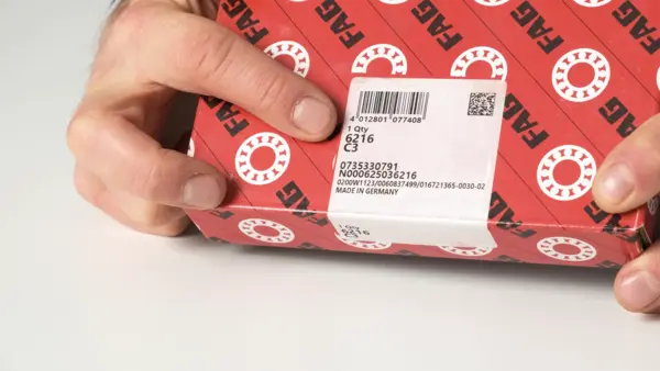 Eine Hand zeigt auf eine rot-weiße Verpackung mit FAG-Logo und aufgeklebtem Produktetikett.
