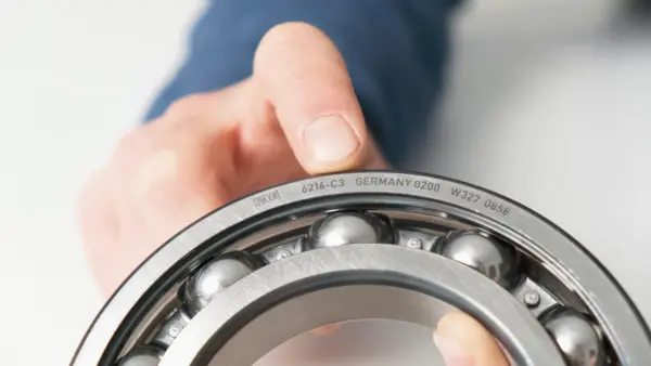 Eine Hand hält ein Kugellager, auf dessen Metallring die Modell- und Herkunftsnummer eingraviert ist.