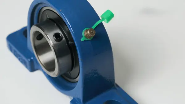 Blaues Stehlager mit eingesetztem Kugellager und Schmiernippel, abgedeckt mit grünem Kunststoffdeckel.