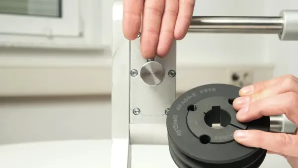 Eine Person setzt eine Keilriemenscheibe mit Taperbuchse auf eine Metallwelle in einer Montagevorrichtung.