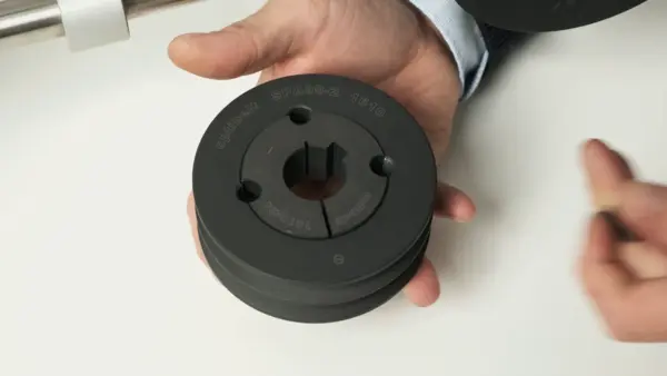 Eine Person hält eine schwarze Keilriemenscheibe mit Taperbuchse in der Hand, die zur Befestigung auf einer Welle dient.