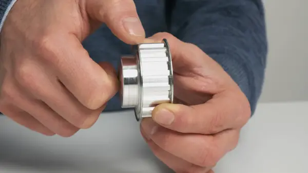 Person zeigt eine silberne Riemenscheibe mit Zähnen, die für Zahnriemen geeignet ist.