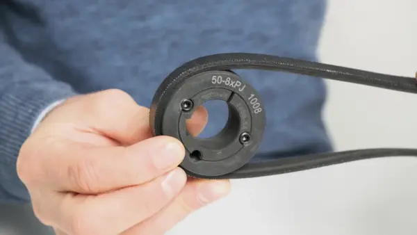 Hand hält eine montierte Riemenscheibe mit aufgezogenem Keilriemen, auf der die Beschriftung ‚50-8xP 1008‘ sichtbar ist.