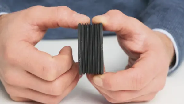 Person hält eine schwarze Riemenscheibe mit mehreren Rillen zwischen den Fingern.