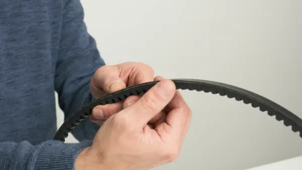 Eine Person hält einen schwarzen Zahnriemen in den Händen und inspiziert die Verzahnung des Riemens.
