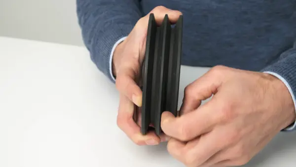 Person hält eine schwarze Riemenscheibe mit mehreren Rillen in beiden Händen.